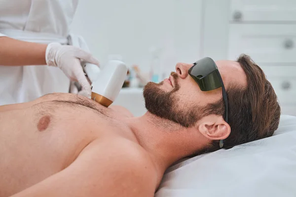 Depilación láser del pecho de un hombre cuidado del cuerpo masculino un  hombre con gafas protectoras y el pecho desnudo se somete a un  procedimiento de depilación láser en una clínica