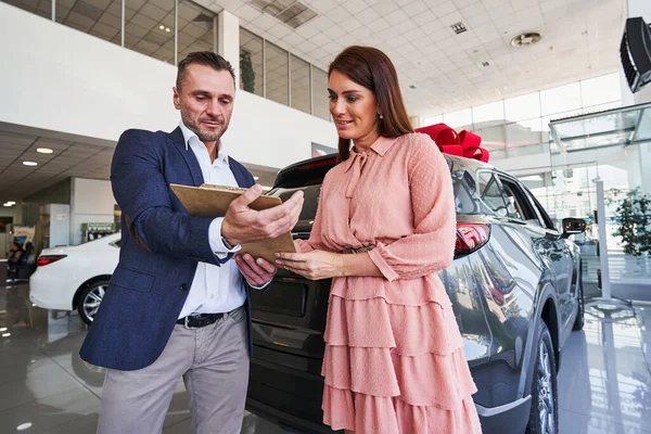 Female customer checking the documents in car dealership — Stock Photo, Image