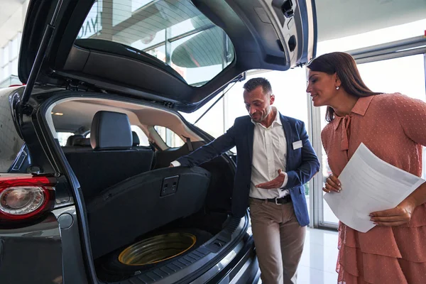 Curious lady looking at the car trunk and smiling — Stock Photo, Image