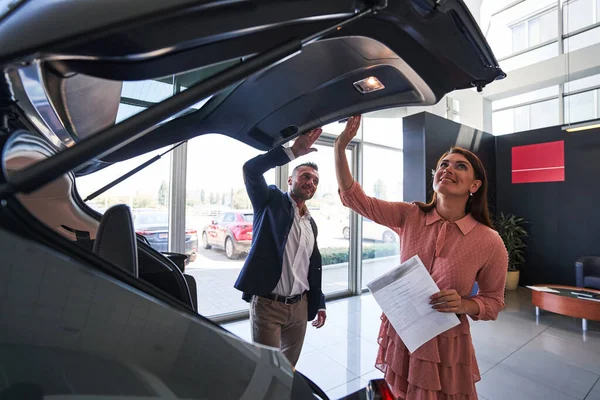 Two cheerful people opening the car in modern showroom — Stock Photo, Image