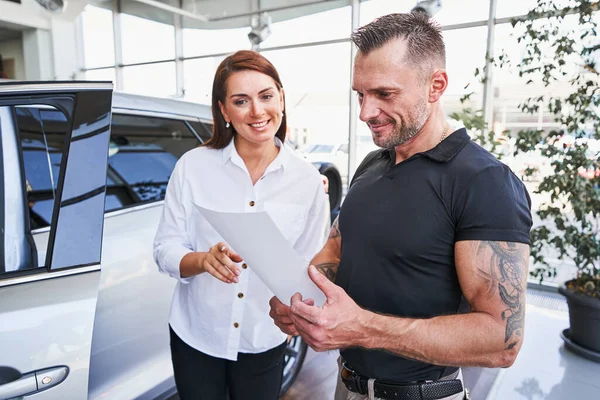 Zufriedener Kunde beim Blick auf die Unterlagen im Autohaus — Stockfoto