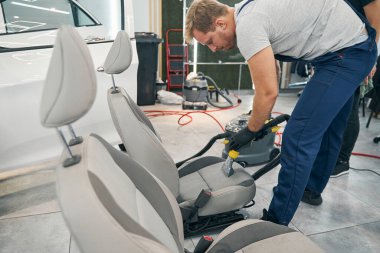 Teknisyen araba servisi merkezinin ön koltuğunu süpürüyor