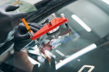 Atölyedeki tamirci kırık arabanın camını elektrikli süpürgeyle tamir ediyor.