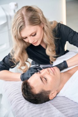 Güzellik kliniğinde genç bir adam için yüz gerdirme ameliyatı yapan kadın.