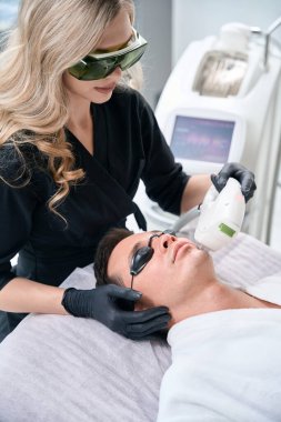 Estetik kliniğindeki genç adam için lazer yüz epilasyonları prosedürü