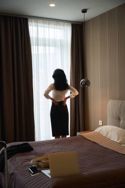 Otel misafiri pencerenin yanında duruyor. Şık seyahat kıyafetleri giyiyor..