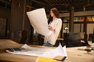 Genç bayan, bir konferans odasında çizimlerle çalışıyor. Evin içinde, şık bir iç mekanda.