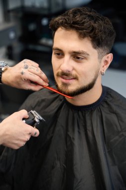 Profesyonel stilistin yakın plan fotoğrafı, yanında duran, elinde saç makası ve sakal kesen bir erkek.