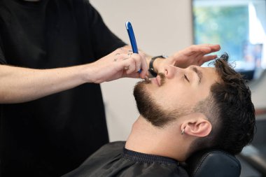 Profesyonel berberin yakın plan fotoğrafı, adamın yanında duruyor, elinde jilet ve tıraş sakalı var.