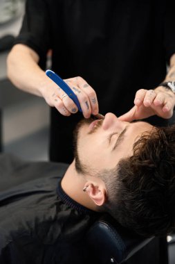 Profesyonel berberin yakın plan fotoğrafı, müşterinin yanında duruyor, küçük jilet tutuyor ve sakal kesiyor.