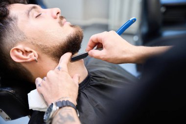 Yetenekli berberin yakın plan fotoğrafını çek, müşterinin yanında dur, sakalını ustalıkla tıraş et.