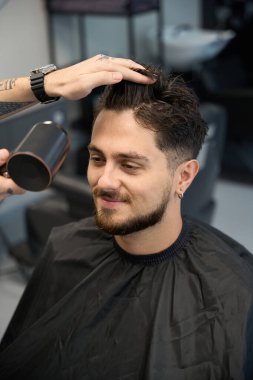 Kuaför, adamın yanında duruyor, saç kurutma makinesi tutuyor ve saç kurutuyor.