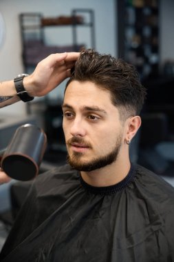 Berber, saç kurutma makinesi ve saç kurutma makinesi tutan adamın yanında duruyor.