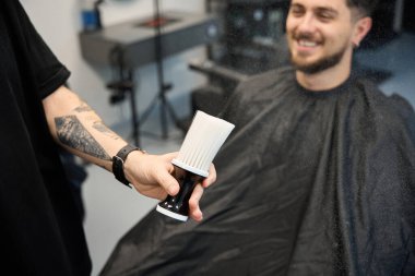 Profesyonel berber, gülümseyen müşterinin yanında duruyor, elinde beyaz tozla büyük bir fırça tutuyor.