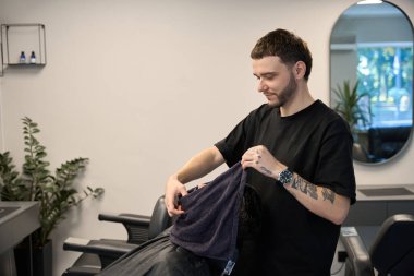 Profesyonel stilist müşterinin yanında duruyor, havluyu tutuyor ve tıraş olmadan önce deri buharı yapıyor.