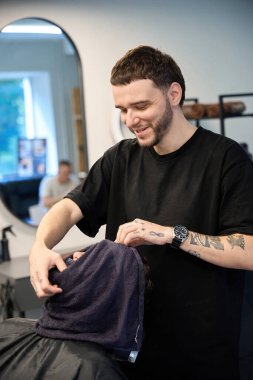 Profesyonel saç kesicisi müşterinin yanında duruyor, havluyu tutuyor ve tıraş olmadan önce deri buharı yapıyor.