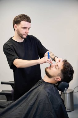 Yetenekli berberin portresi, müşterinin yanında duruyor, ustalıkla tıraş edilmiş adam sakalı ve küçük jilet.