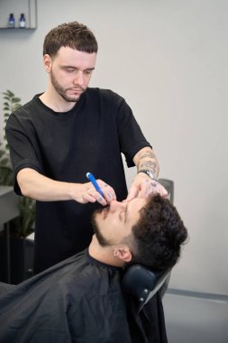 Yetenekli berberin portresi, erkeğin yanında duruyor, ustalıkla tıraş edilmiş adam sakalı ve küçük jilet.