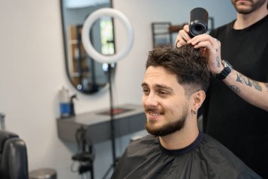 Berber, gülümseyen müşterinin yanında duruyor, saç kurutma makinesi tutuyor ve saçını kurutuyor, saç şekillendiriyor.