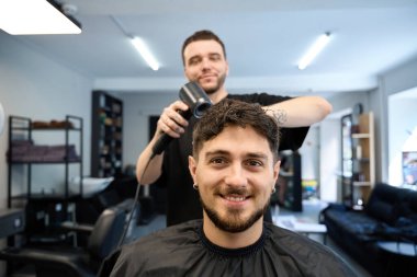 Profesyonel kuaför, gülümseyen müşterinin yanında duruyor, saç kurutma makinesi tutuyor ve saç kurutuyor, saç şekillendiriyor.