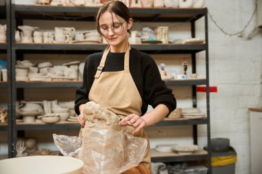 Seramik stüdyosunda çalışan kadın çömlekçi, kil paketi açıyor.