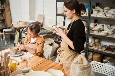 Tatlı yaşlı bayan atölyesinde kilden kase yapıyor. Bir ustanın gözetiminde çalışıyor.