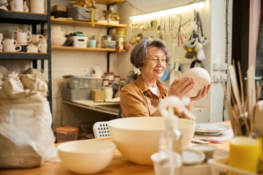 Emeklinin biri seramik stüdyosunda kase yapıyor, yanında da özel aletler var.