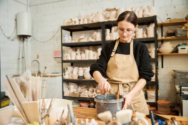 Sanatçı kadın cilalamak için özel bir çözüm hazırlıyor, bir kadın seramik stüdyosunda çalışıyor.