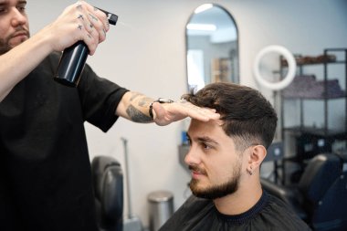 Profesyonel berberin elinde sprey şişesiyle yakın plan fotoğrafı.