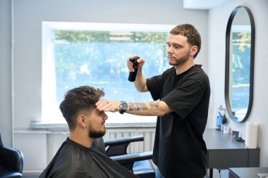 Profesyonel bir adam elinde sprey şişesi tutuyor ve saç kesimine ürün uyguluyor.