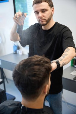 Profesyonel erkek sprey şişesi tutuyor ve saç kesimine ürün sürüyor.