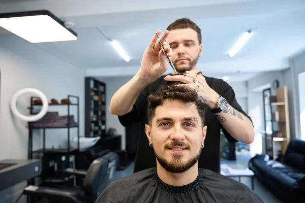 Profesyonel berber mutlu bir adamın yanında duruyor, elinde makas tutuyor ve saç kesiyor, saçını kesiyor.