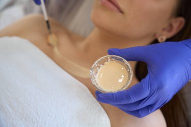 Kozmetik uzmanının tedavi için genç bir kadının yüzüne nemlendirici maske takması, cilt bakımı. Yüz bakımı, cilt bakımı, kozmetoloji konsepti.