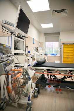 Steril bir hastane odasında tıbbi malzemeler sergileniyor. Özellikler, monitörler, solunum cihazları, serum direkleri ve kayışlı ve başlıklı hasta sedyesi, sakin ve verimli bir atmosfer yaratıyor..