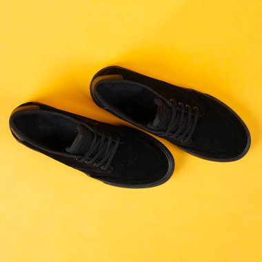 Mor tabanlı sade siyah spor ayakkabılar. Sarı arka plandaki Plimsoll ayakkabılar fotoğrafa iyi bir etki yapar. Ön cephede. Yan atış. Sarı arkaplanda spor ayakkabıları tutan eller.                               