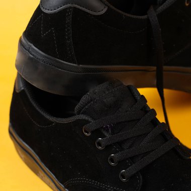 Mor tabanlı sade siyah spor ayakkabılar. Sarı arka plandaki Plimsoll ayakkabılar fotoğrafa iyi bir etki yapar. Ön cephede. Yan atış. Sarı arkaplanda spor ayakkabıları tutan eller.                               