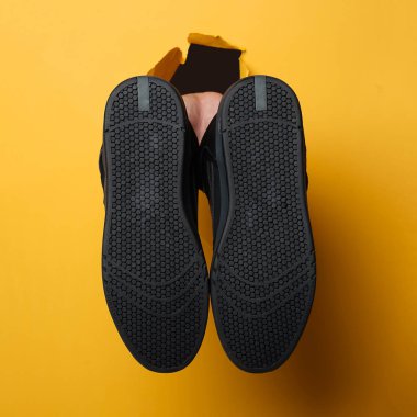 Adamın sağ eli sarı kağıttan bir çift ayakkabı tutuyor. Reklam içeriği için alanı kopyala. En iyi seçim konsepti. Duvar kağıdındaki delikler. Yaratıcı reklam alanının maketi. Spor ayakkabılar.