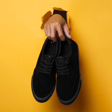 Mor tabanlı sade siyah spor ayakkabılar. Sarı arka plandaki Plimsoll ayakkabılar fotoğrafa iyi bir etki yapar. Ön cephede. Yan atış. Sarı arkaplanda spor ayakkabıları tutan eller.                               