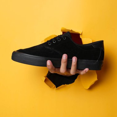 Mor tabanlı sade siyah spor ayakkabılar. Sarı arka plandaki Plimsoll ayakkabılar fotoğrafa iyi bir etki yapar. Ön cephede. Yan atış. Sarı arkaplanda spor ayakkabıları tutan eller.                               