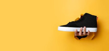 Adamın sağ eli siyah bir ayakkabı tutarken sarı kağıt duvardan geçmiş. Pankart tasarımı kadar uygun. Üçüncü Kural 'ı kullanan fotoğrafların kompozisyonu. Reklam.