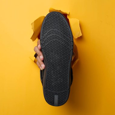 Sağ insan eli, siyah spor ayakkabı tutarak sarı kağıt duvarı yardı. Erkek eli spor ayakkabısı tutuyor. Spor ayakkabıları tutan ellerin modeli. Reklam ihtiyaçlarınız için uygun. Güzel ayakkabılar.                               