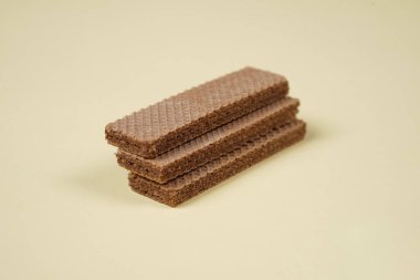 Sarı arka planda izole edilmiş rastgele bir yığın gofret. Çikolatalı bisküviler lezzetli kremalı çikolatalarla dolu. Kuru ve çıtır gofretler yemeye hazır. Güne bir gofretle başlamaya hazırım..