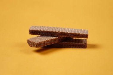 Sarı arka planda izole edilmiş rastgele bir yığın gofret. Çikolatalı bisküviler lezzetli kremalı çikolatalarla dolu. Kuru ve çıtır gofretler yemeye hazır. Güne bir gofretle başlamaya hazırım..