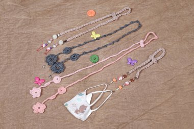 Kayıp ya da unutulmasın diye kumaş maskeyi boncuklu ya da elle örülmüş kayışlarla asmak. Sağlık maskesi takmamızı kolaylaştıran kayışlar. Boncuk kayışlar, el örgüsü kayışlar..    