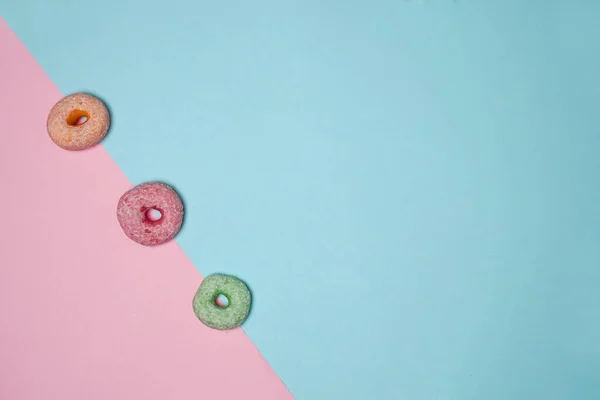 Three donuts of varying colors line neatly between the pink and blue background borders. delicious snacks suitable to be eaten in spare time. Practical mini donuts to carry wherever you are.