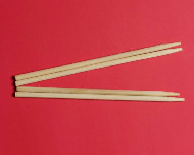 Kırmızı arka planda bambudan yapılmış bir çift çubuk. Bambu çubukları genellikle erişte ve suşi şeklinde yemek yemek için kullanılır. Oluşturulan bambu çubukları uçlarında inceltilmiştir..