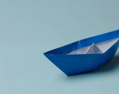 Mavi arka planda mavi tekne şekilli origami. Origami oynamak düşünme gücünün artmasına ve çocukların yaratıcı yeteneklerinin artmasına yardımcı olur. Origami oynamak çocuklar için alternatif bir öğrenme olabilir..