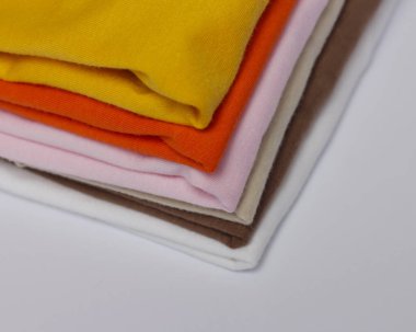 Renkli düz giysi yığını. Parlak bir arkaplanda düzgün düzenlenmiş tişört modeli. Düzgünce düzenlenmiş kıyafetlerin üst görüntüsü. Pamuk kumaştan düz tişörtler sergilenmeye hazır..