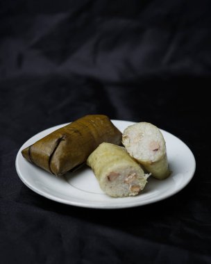 Lepet kek siyah arka planda izole. Kue lepet, yer fıstığıyla karıştırılmış, hindistan cevizi sütüyle pişirilmiş ve muz yapraklarına sarılmış glutinöz pirinçten yapılır. Lepet kek tipik bir Endonezya pastasıdır. Odak bulanıklığı.