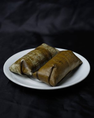 Lepet kek siyah arka planda izole. Kue lepet, yer fıstığıyla karıştırılmış, hindistan cevizi sütüyle pişirilmiş ve muz yapraklarına sarılmış glutinöz pirinçten yapılır. Lepet kek tipik bir Endonezya pastasıdır. Odak bulanıklığı.